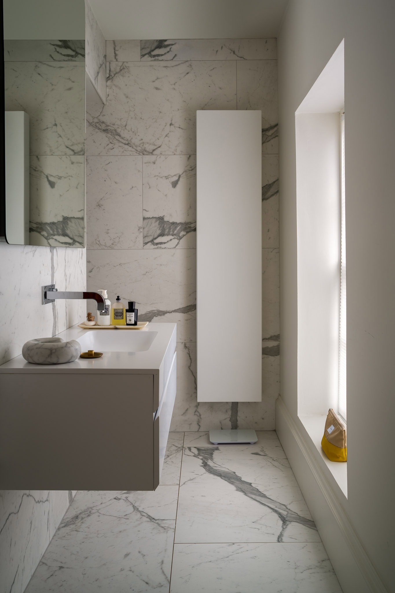 Clean modern bathroom with marble tiles, white vanity, and natural light from a large window.
