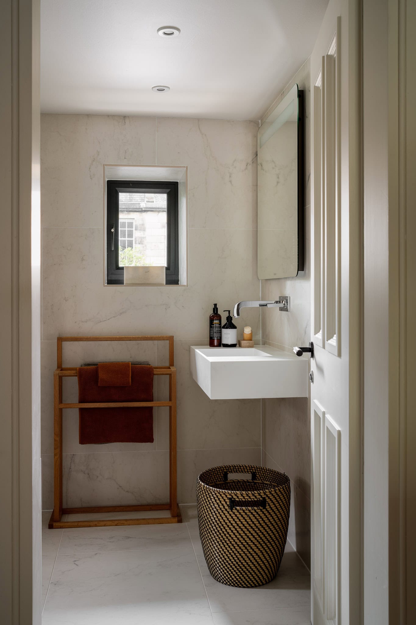 Bright modern bathroom with a white sink, wooden towel rack, and woven laundry basket, featuring min.