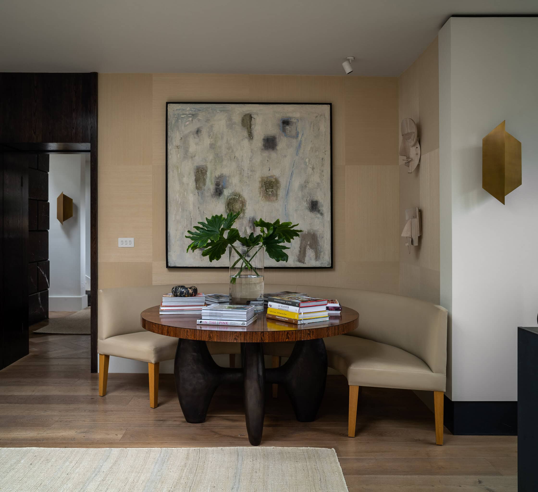 Modern dining nook with round wooden table and beige seating, stylish wall art and decor accents.