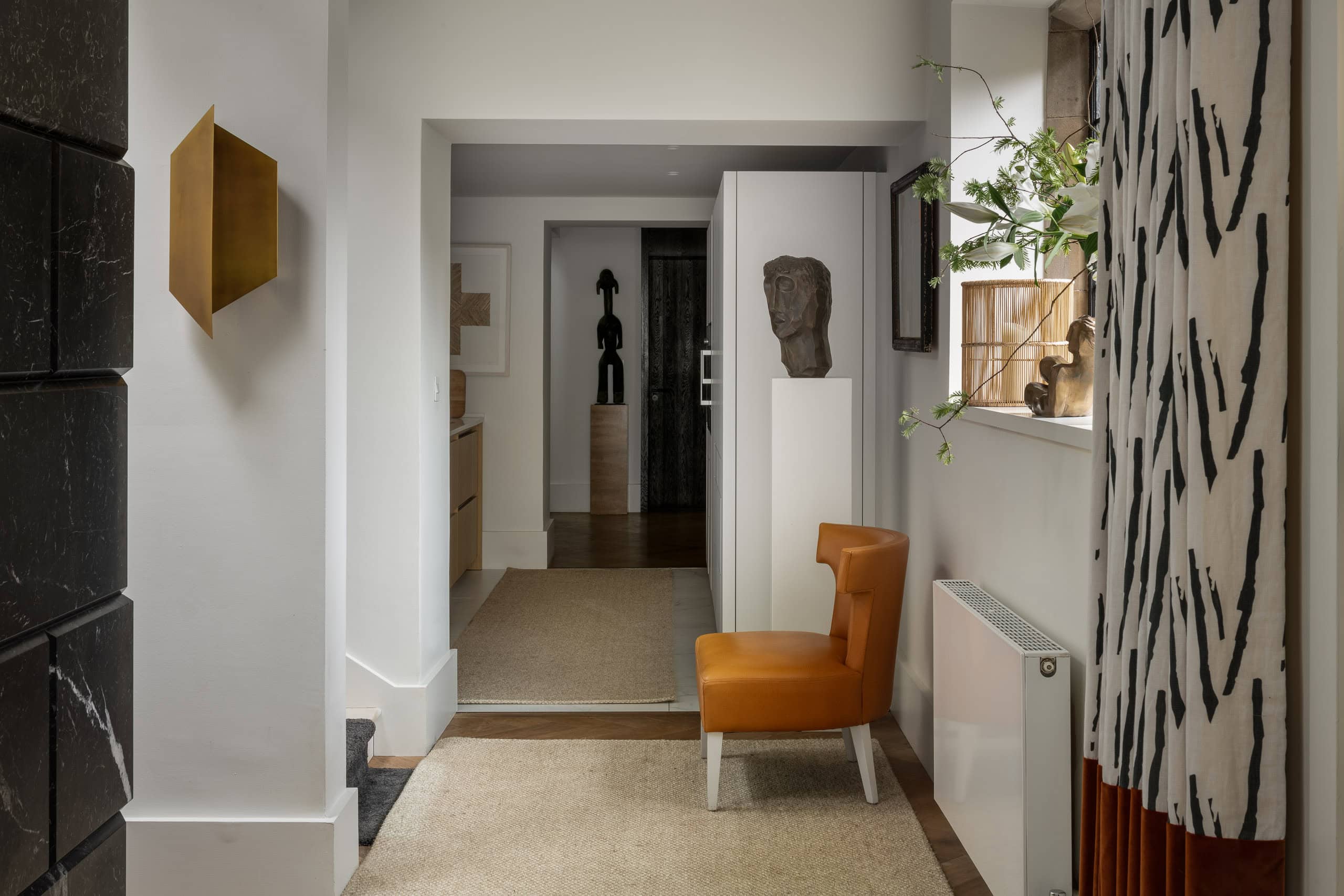 Modern hallway with stylish decor, orange accent chair, and natural light in a contemporary home.