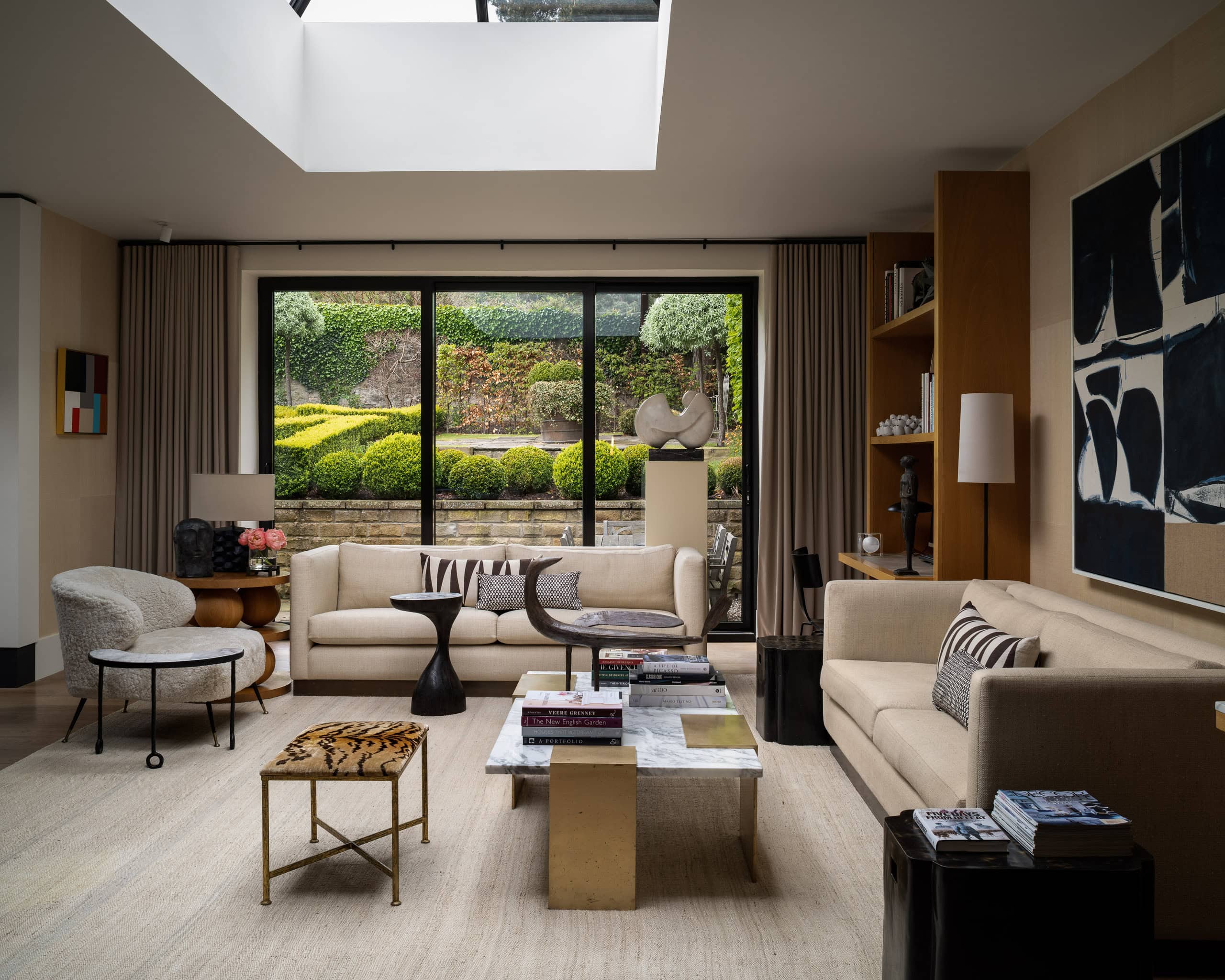 Modern living room with large window overlooking a lush garden, featuring neutral-toned furniture an.