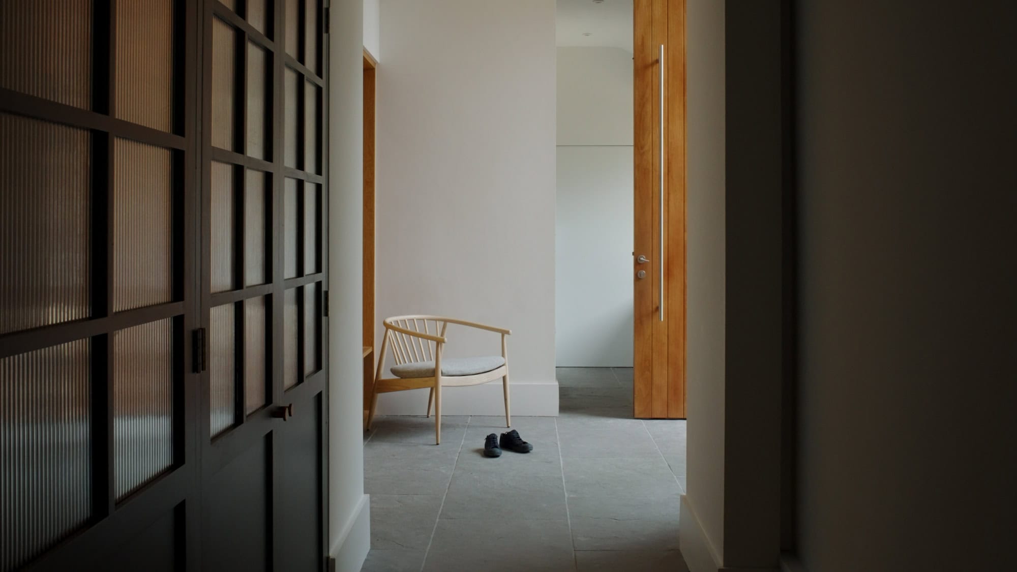 Modern minimalist interior hallway with wooden accents and natural light, showcasing large contemporary front door