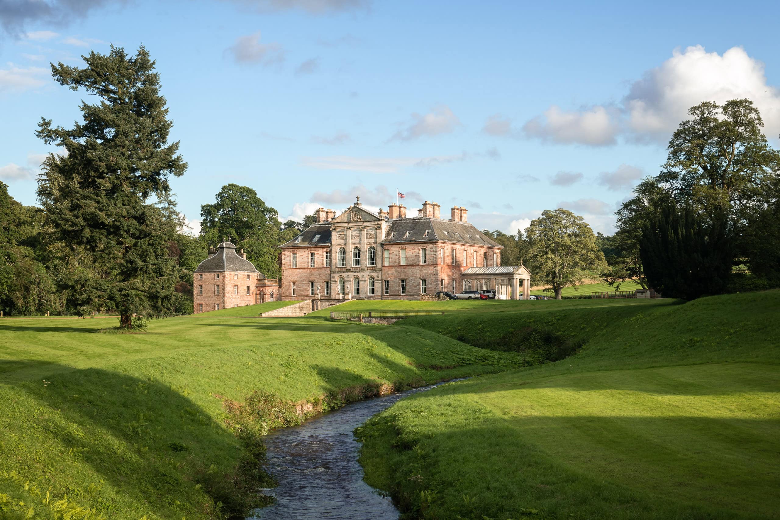 A lush green golf course with a historic mansion in the background under a blue sky.