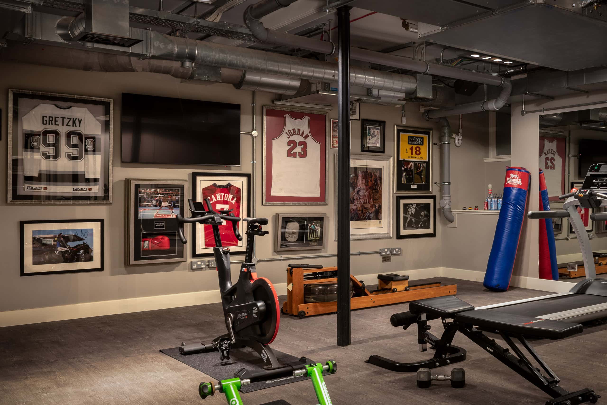Cycling and workout equipment in a home gym with sports memorabilia and framed jerseys on the wall.