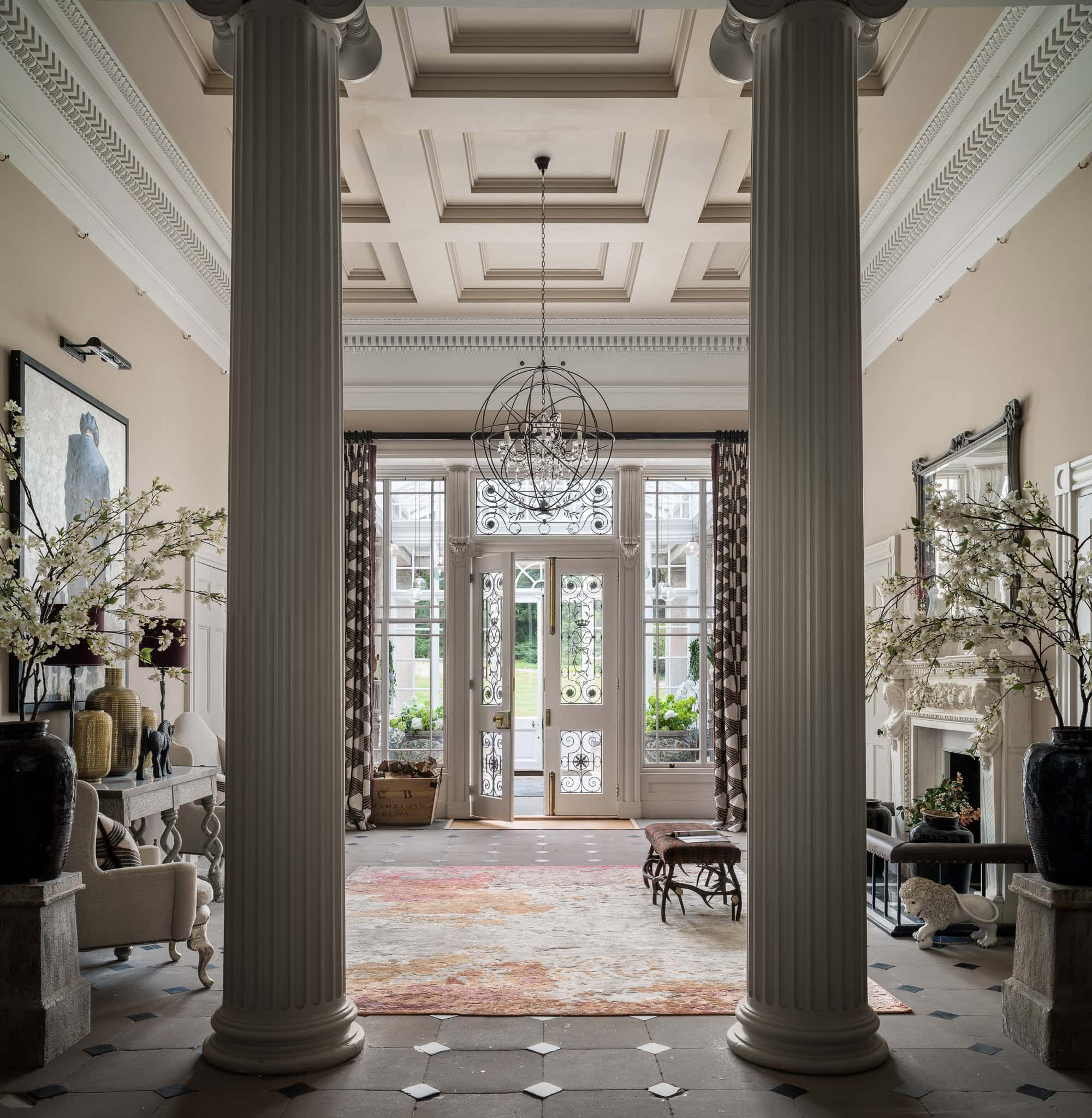 Elegant Victorian-style entrance hall with tall columns, ornate ceiling, and large windows, showcasi.