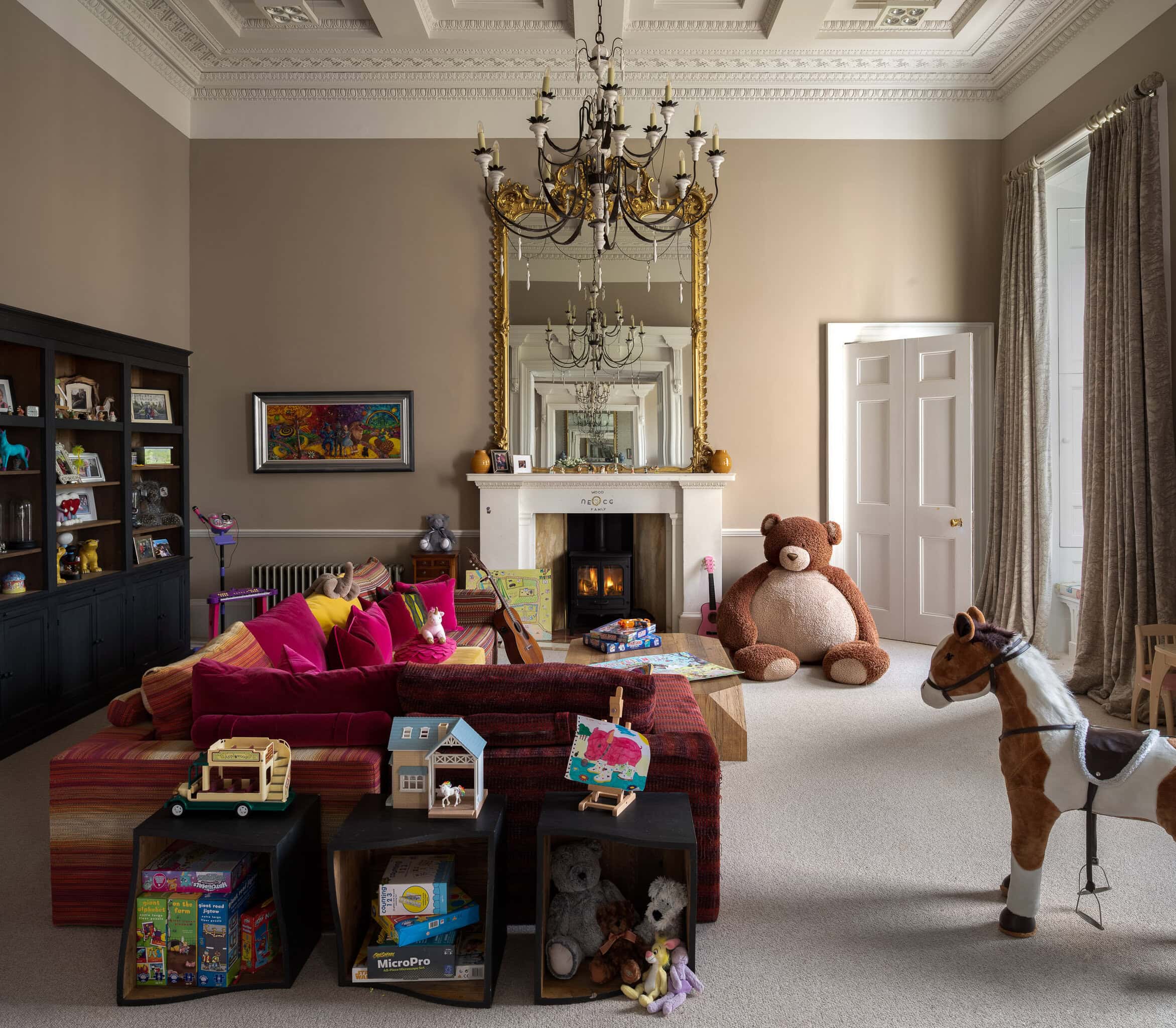 Soft beige living room with fireplace, large mirror, colourful toys, and a giant teddy bear, creatin.