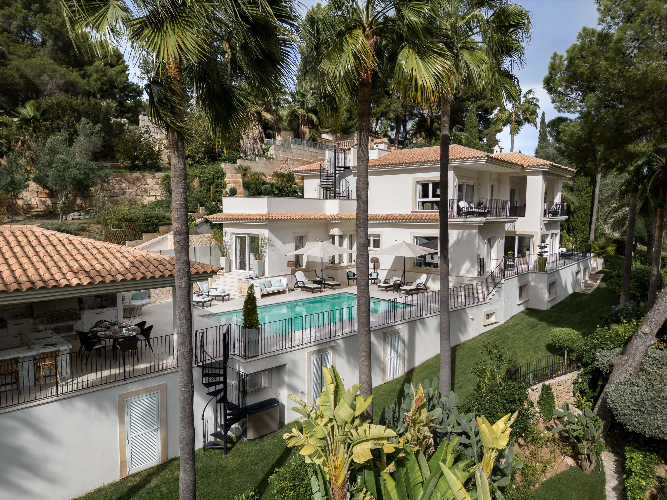 Luxurious modern villa with private pool surrounded by lush greenery and palm trees in a scenic Mallorca