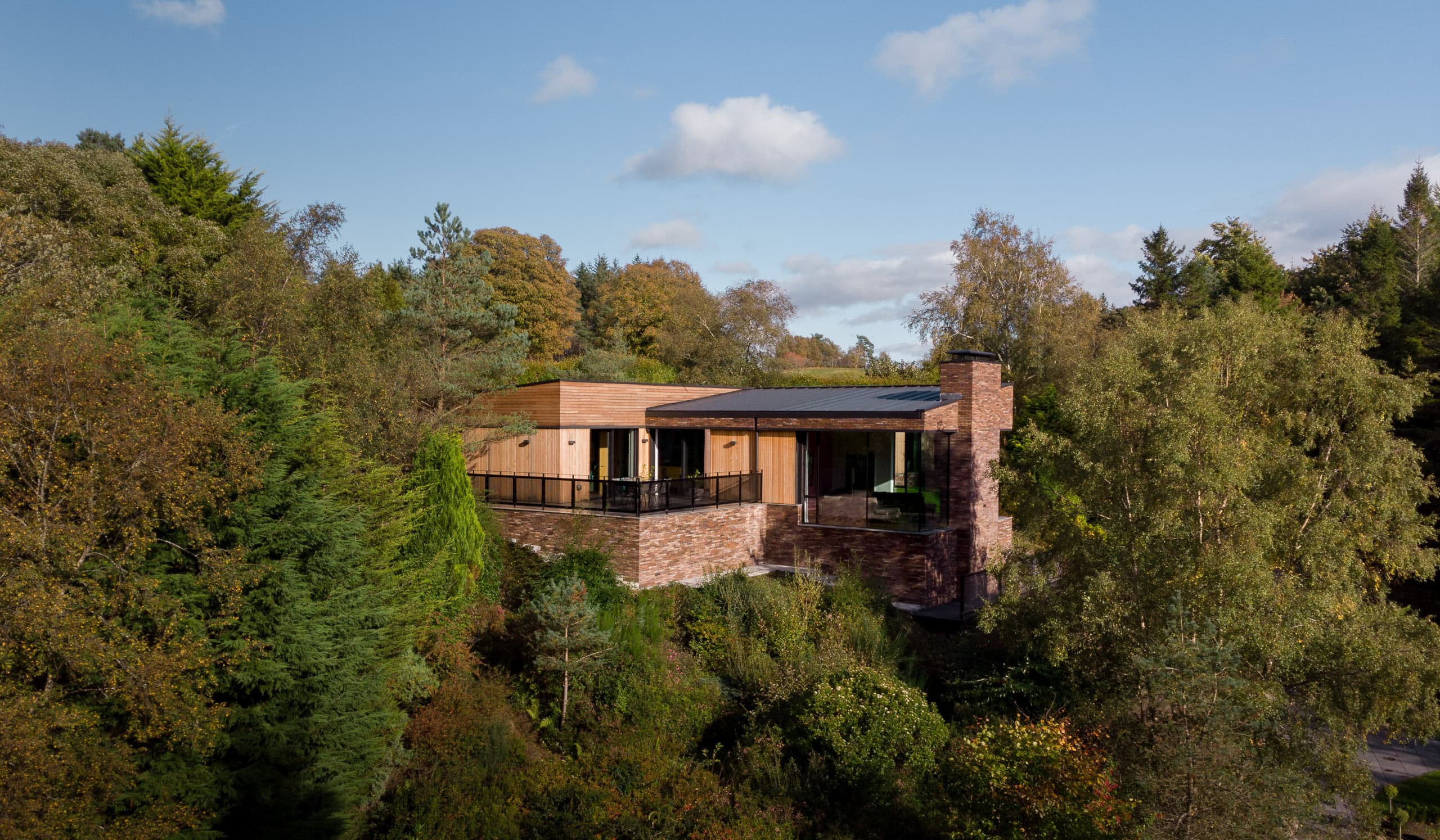 Aerial drone photograph of Pond House by Technique Studio surrounded by dense woodland and landscaped gardens in a secluded natural setting.