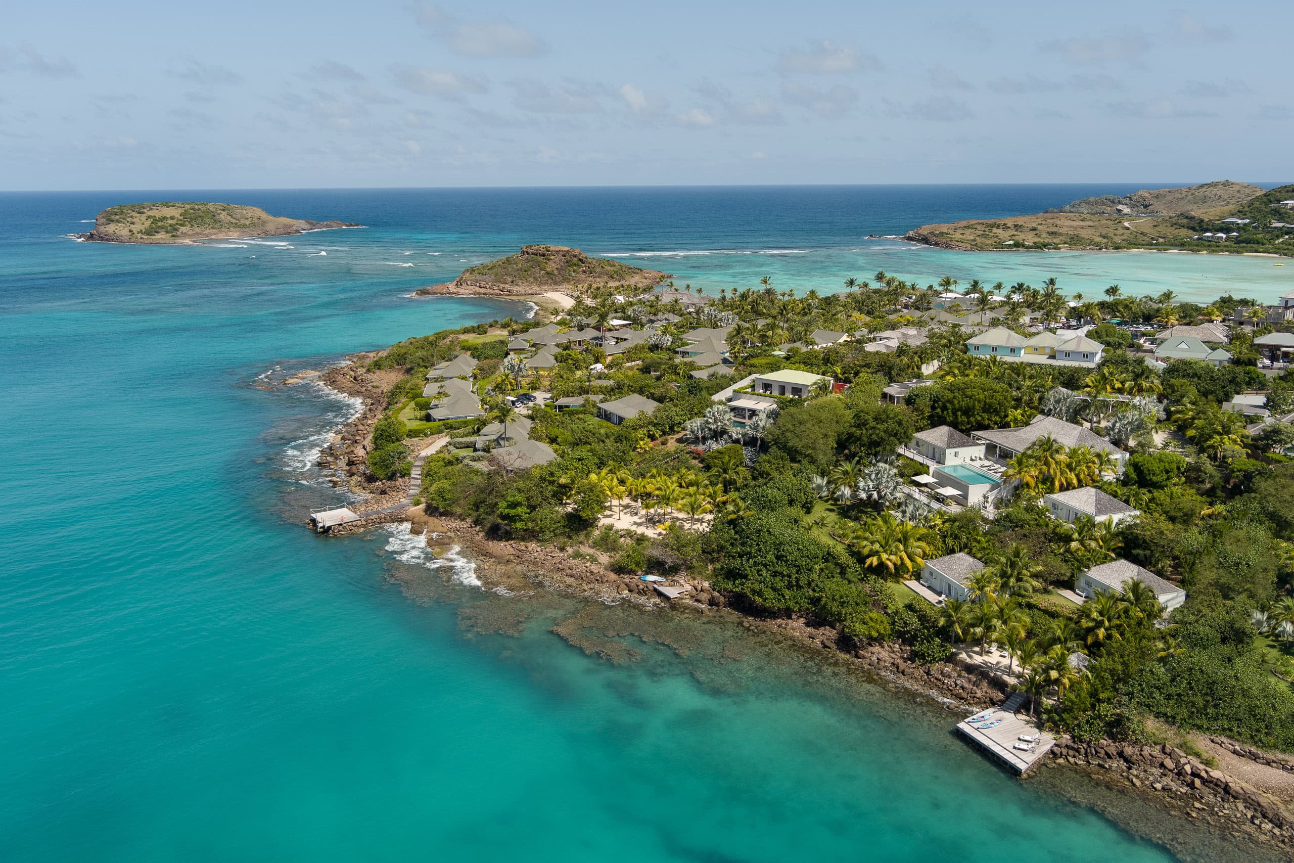 Aerial drone photograph overlooking a tropical bay in St. Barts featuring turquoise Caribbean waters, lush coastal vegetation, and multiple private luxury villas.