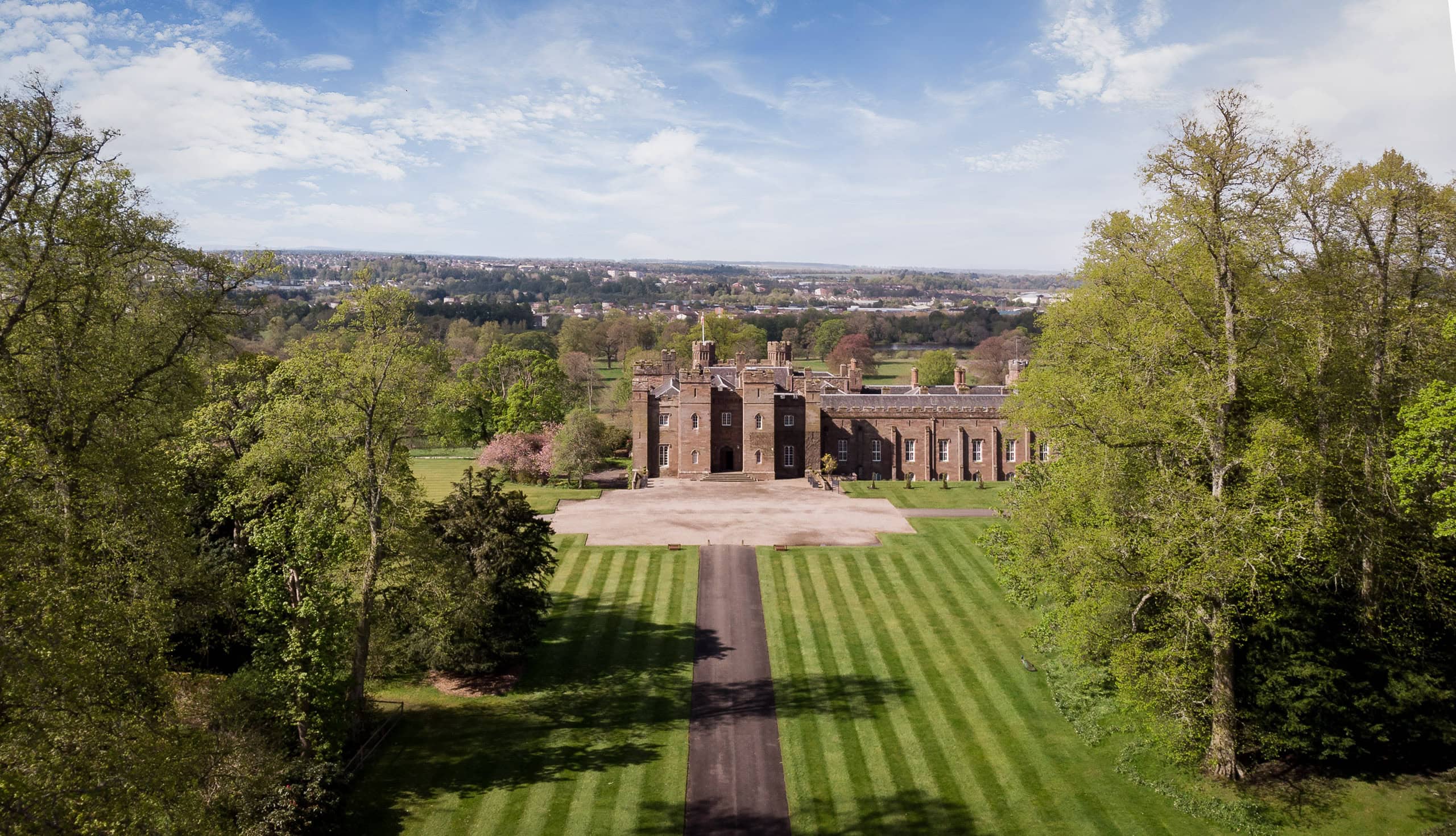 Aerial drone photograph of Scone Palace in Perthshire featuring formal landscaped grounds, tree-lined approach, and expansive views across the surrounding countryside.