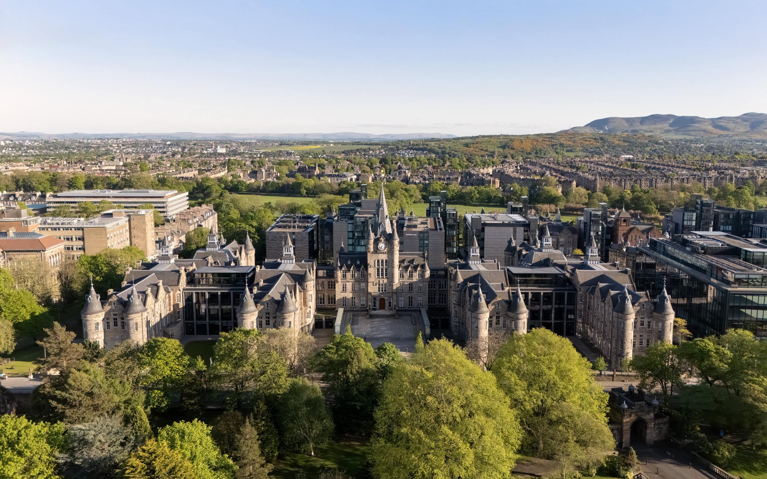 Aerial view of the Edinburgh Futures Institute by Bennetts Associates featuring restored historic stone architecture set against the wider Edinburgh cityscape and surrounding hills.