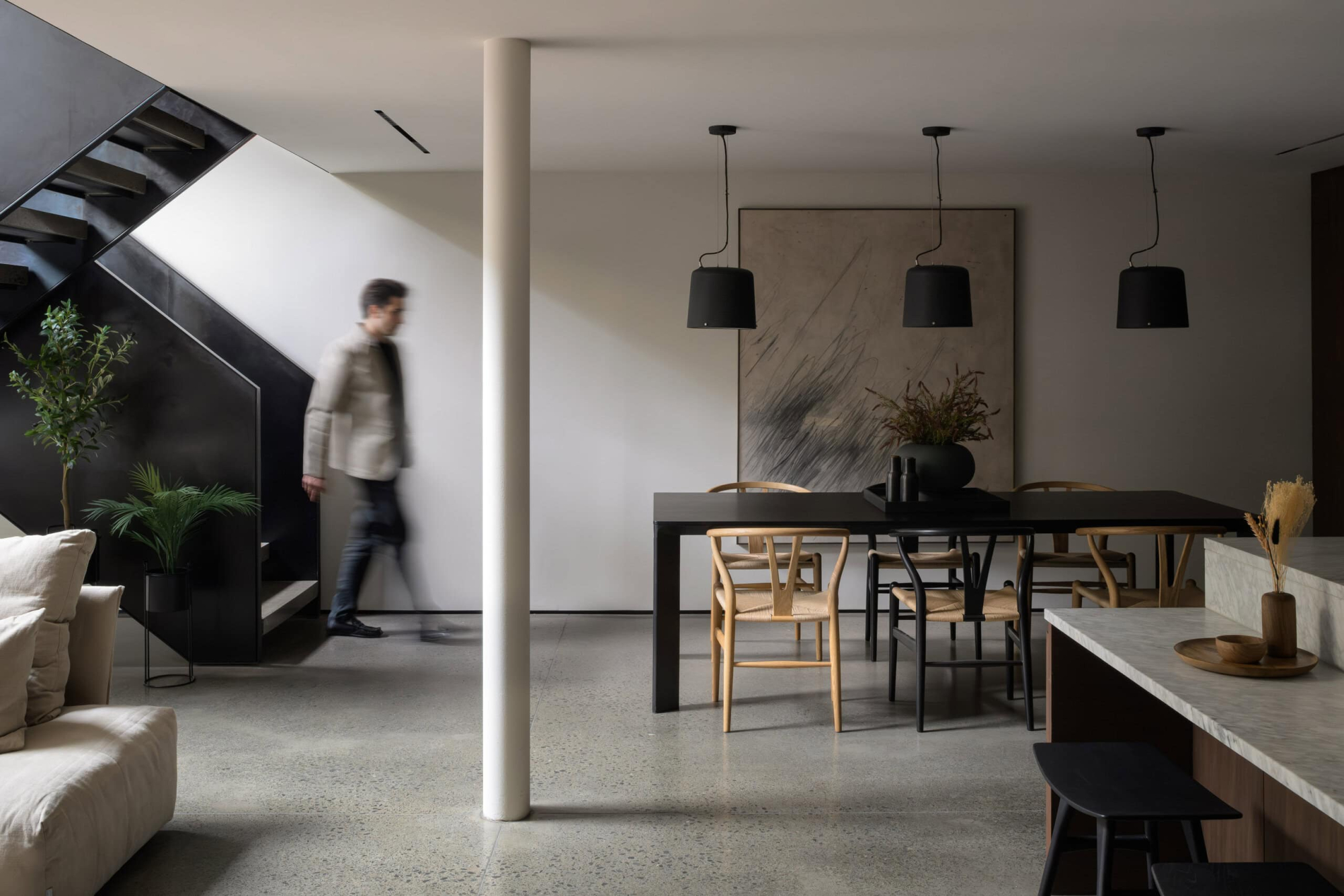 Minimal contemporary dining interior in an Edinburgh townhouse by Morgan Architects featuring polished concrete floors, black staircase detailing, and sculptural pendant lighting.