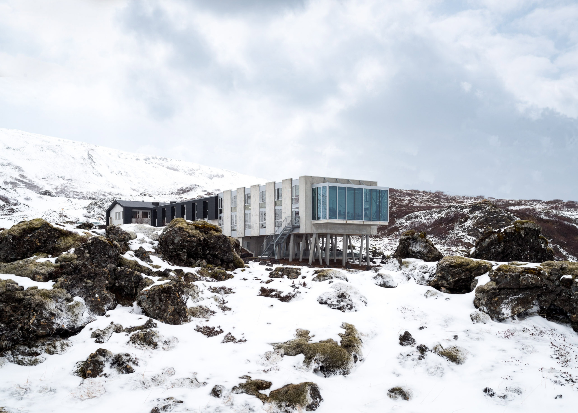 Modern mountain retreat with large glass windows and concrete structure in snowy landscape.