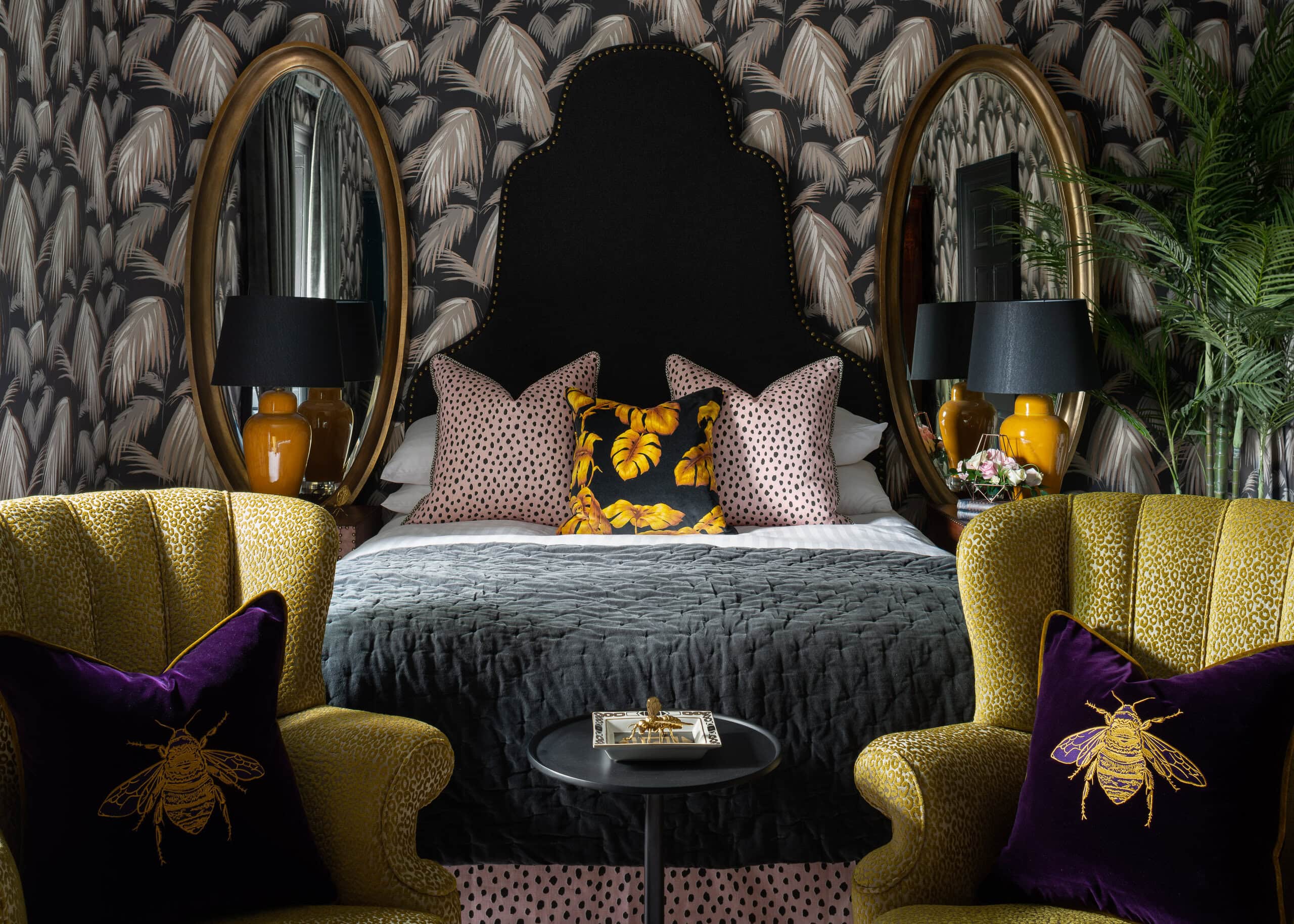 Luxurious bedroom interior at Charlton Hall designed by Jeffreys Interiors featuring patterned botanical wallpaper, black upholstered headboard, oval mirrors, and richly coloured velvet furnishings.