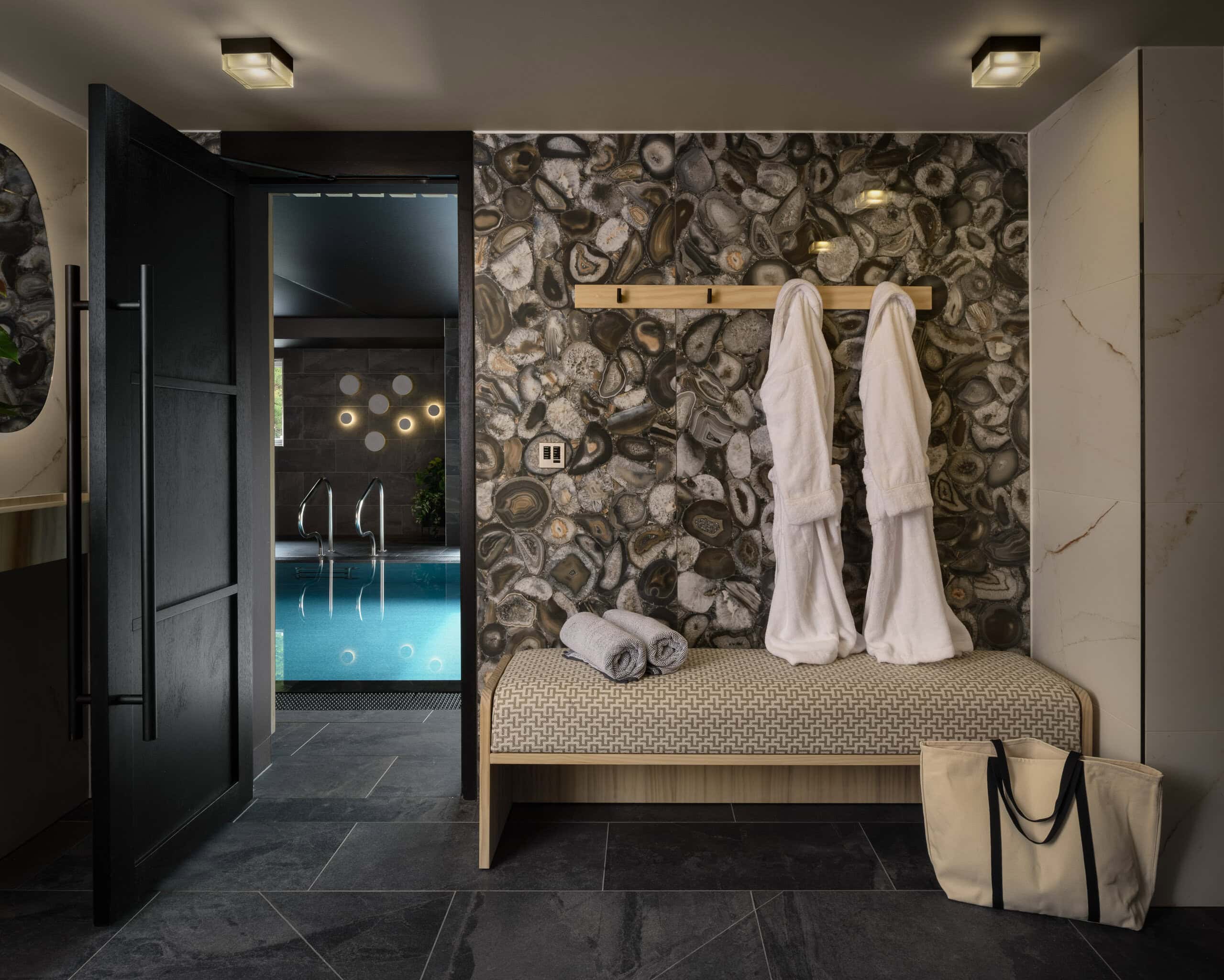 Modern spa room with stone wall, robes, and pool view in the background.