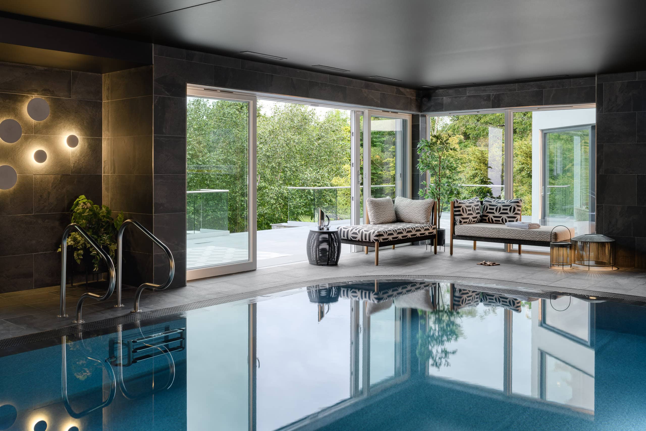 Modern indoor swimming pool with large glass doors and stylish seating area.