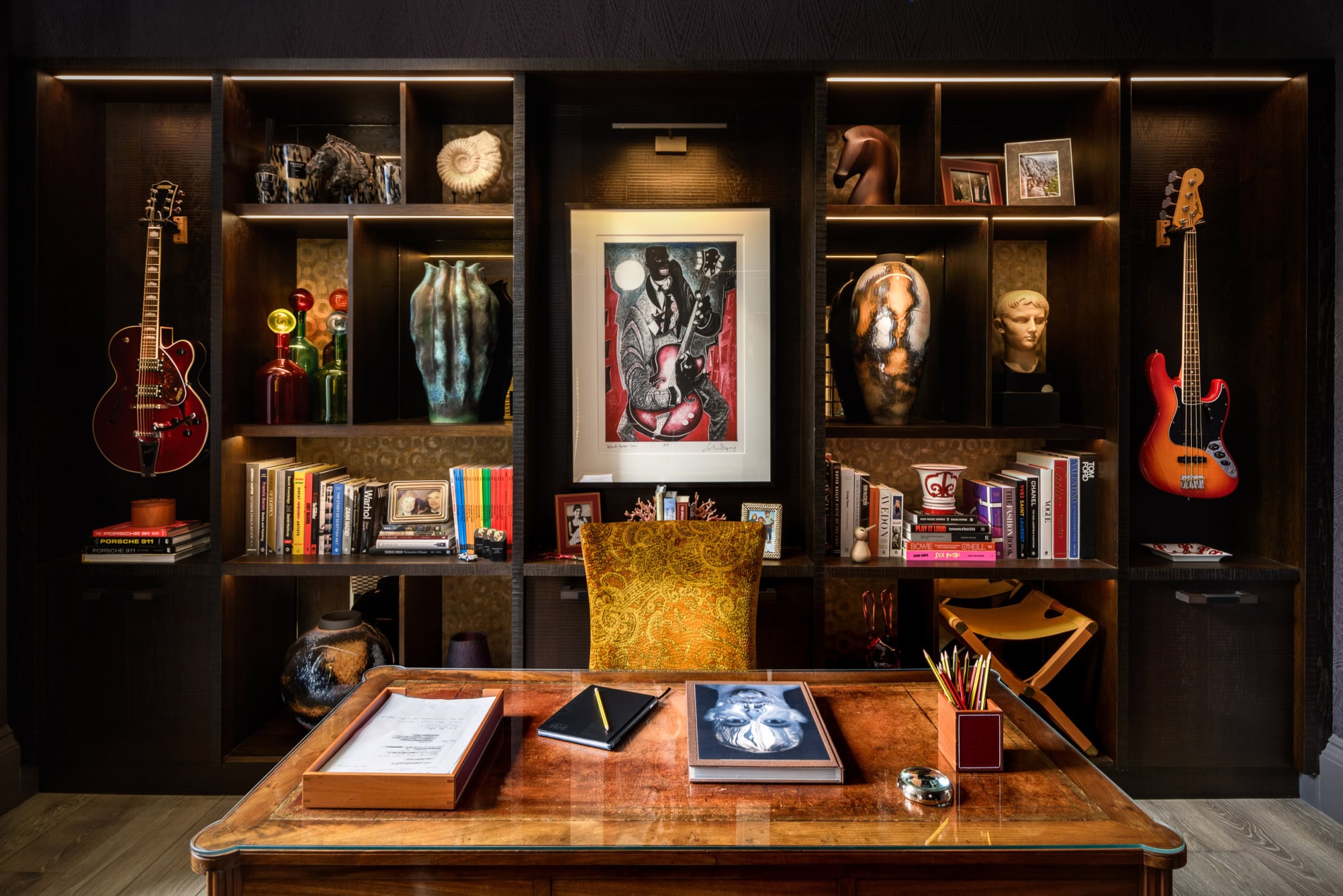 Interior of a stylish home office with bookshelves, guitars, and artwork.