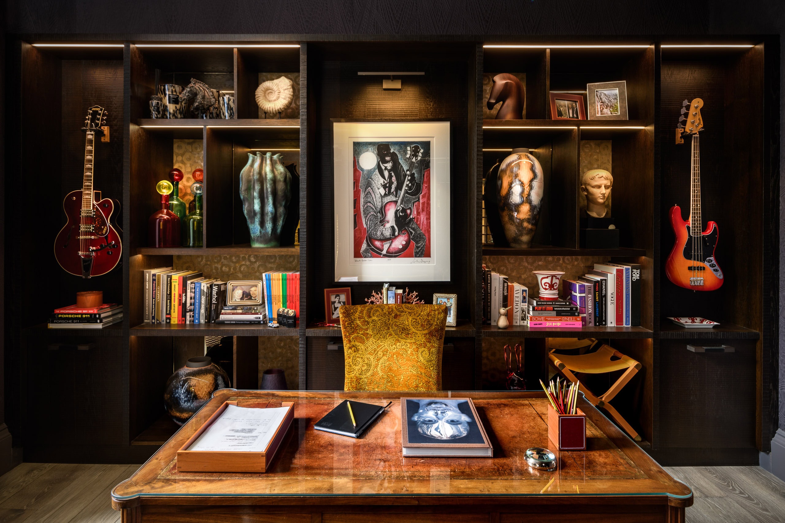 Interior of a stylish home office with bookshelves, guitars, and artwork.