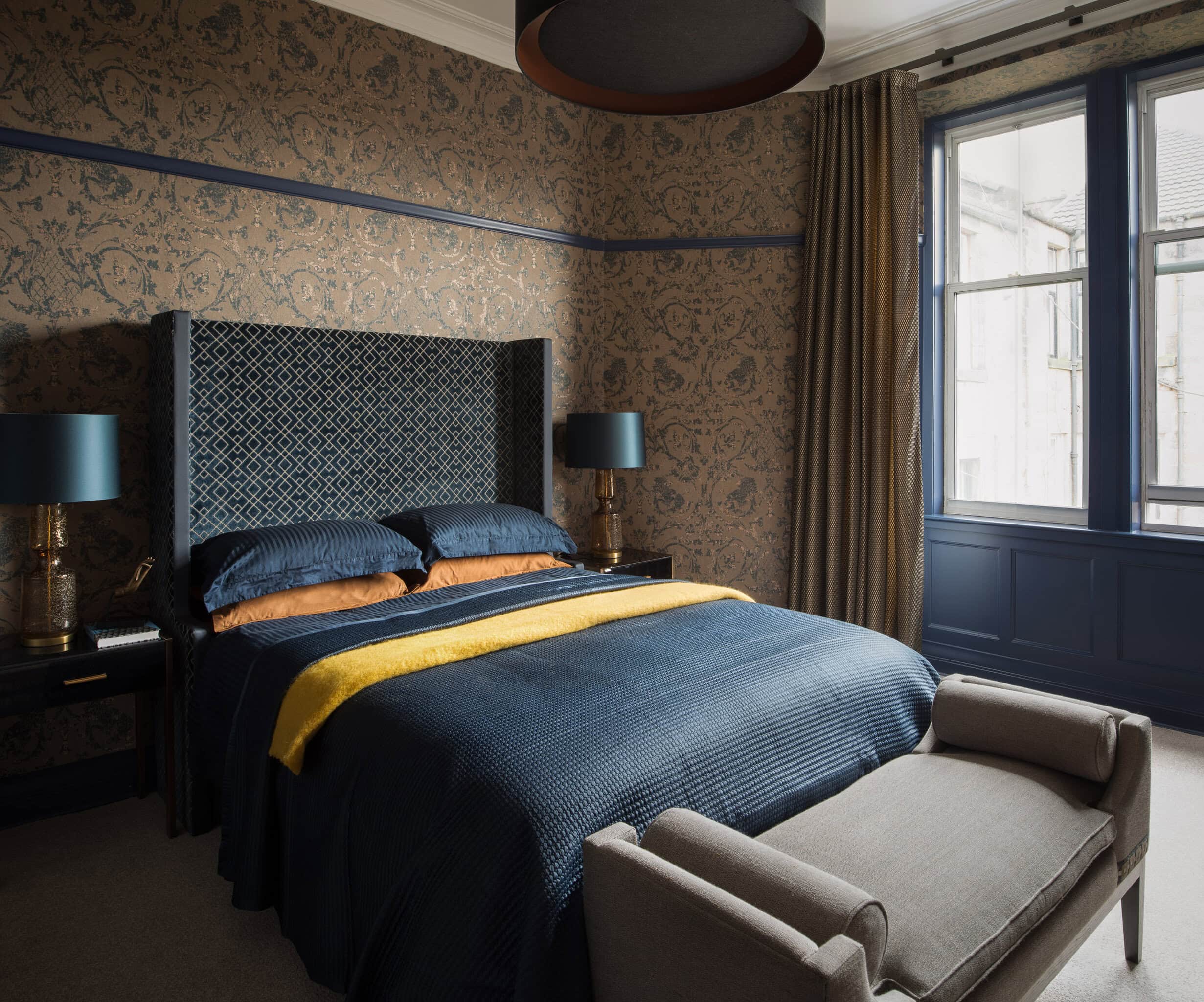 Elegant bedroom with patterned wallpaper, navy bedding, and large window with curtains.