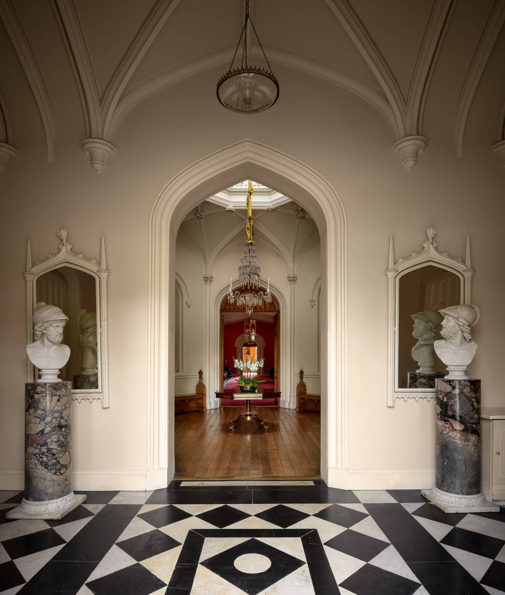 Elegant historic interior with ornate archway and classical busts on marble pedestals.