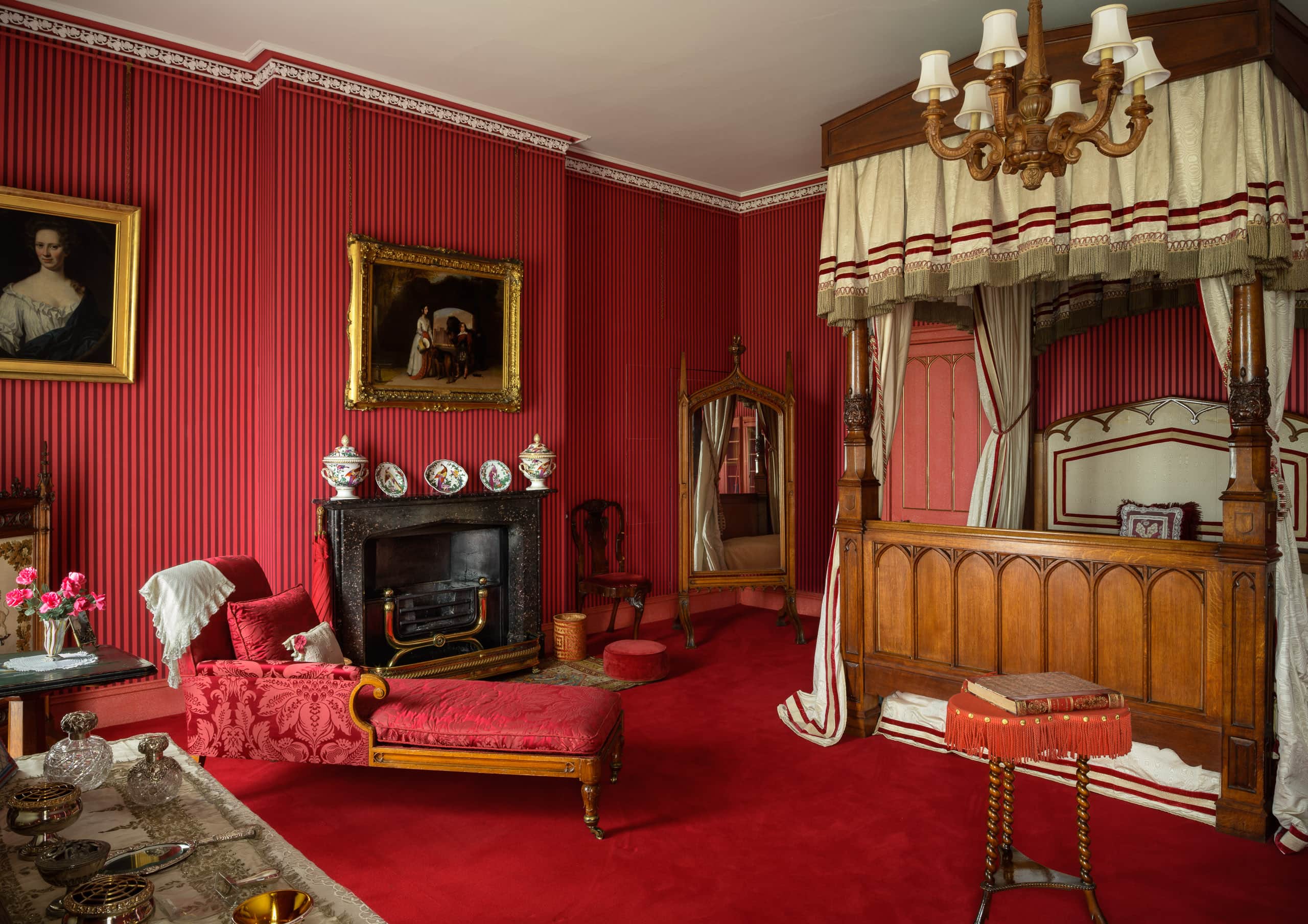 Elegant vintage bedroom with red wallpaper, four-poster bed, and antique furnishings.