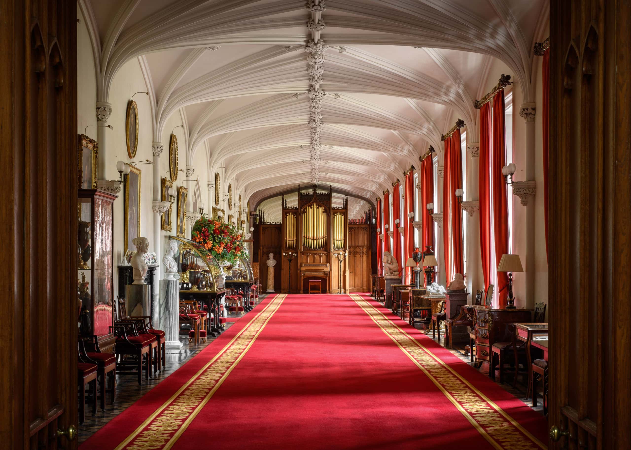Elegant historic corridor with red carpet, ornate ceiling, and vintage furniture.