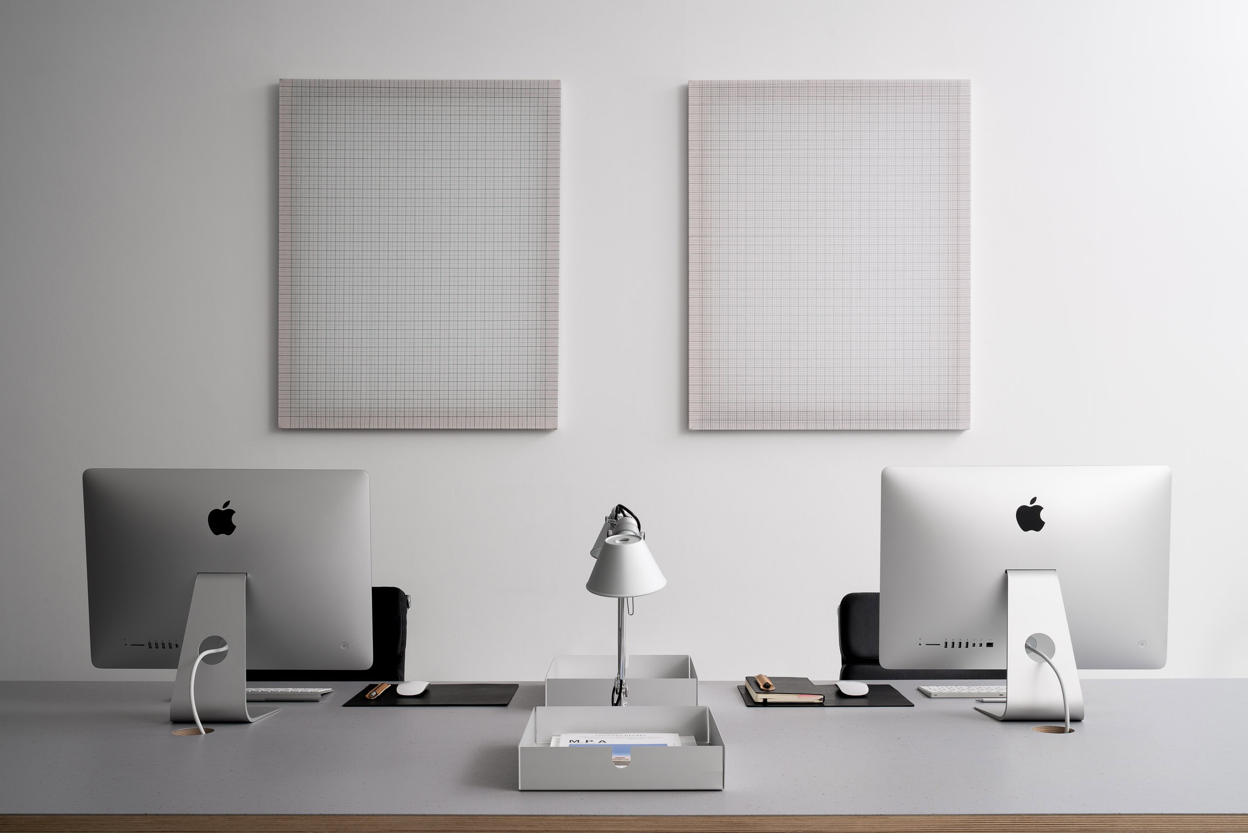 A computer workspace with two iMacs and minimalist decor in a modern office setting.