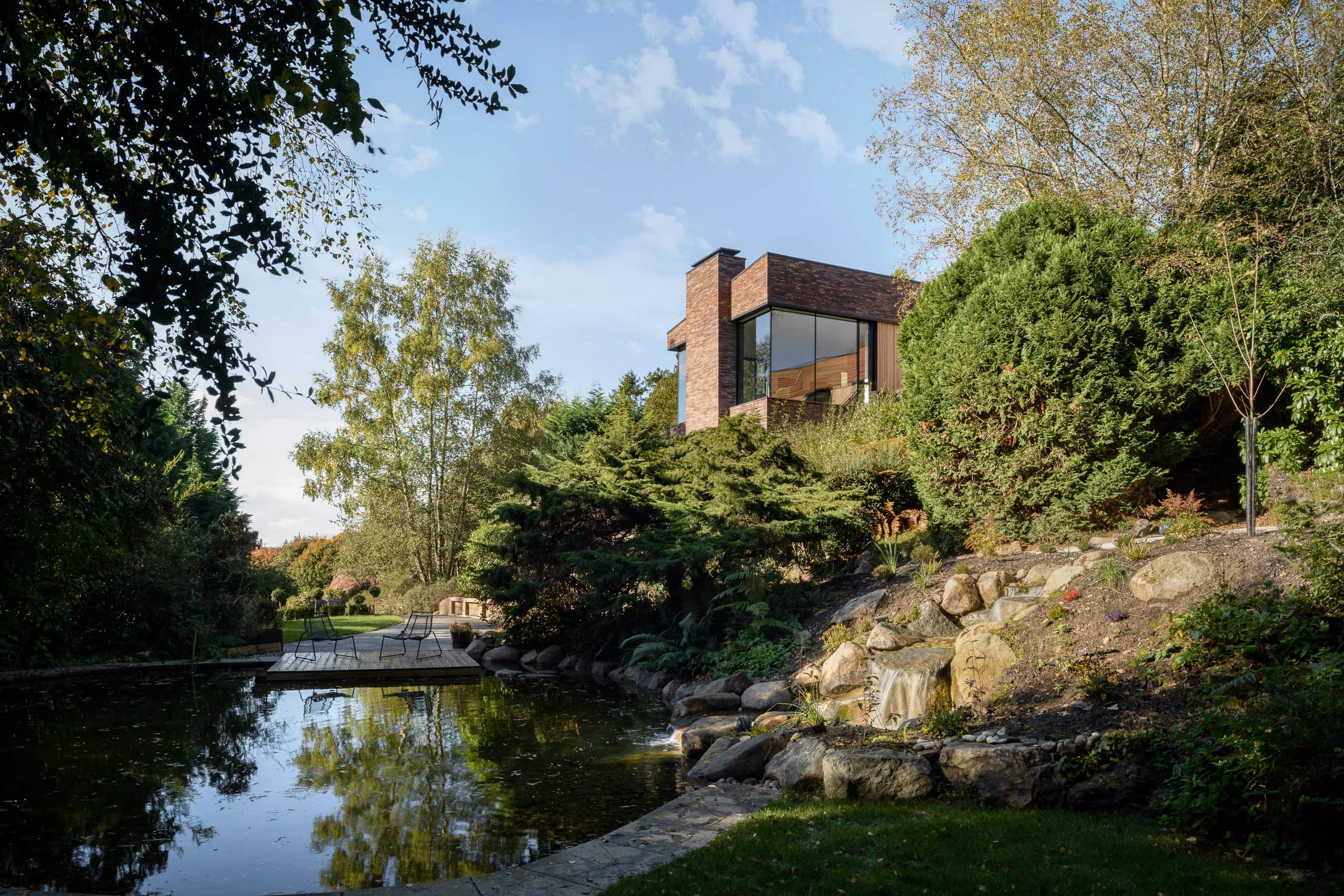 Modern residential house overlooking a pond with lush greenery and natural landscape.